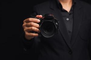 Photographer in a suit holding the digital camera while standing on a black background. photo