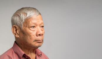 Portrait of an elderly Asian man in a shirt looking away with a smile while standing on a gray background photo