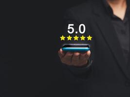 Close-up of Satisfaction and feedback surveys. A businessman in a suit using a smartphone gives the five-star icon a rating of very impressed for service photo