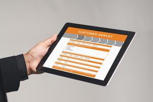 Close-up of a businessman in a suit holding a tablet with a customer survey form while standing on a gray background. photo