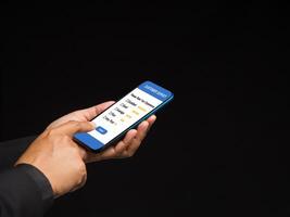 Businessman in a suit using a smartphone with a customer survey form while standing on a black background photo