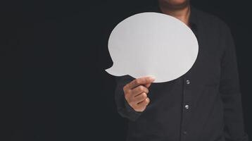 Close-up of a businessman holding a blank white speech bubble while standing on a black background photo
