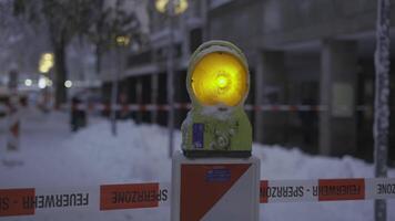 Street in Munich, Germany, is closed due to heavy snowfall. A flashing warning light and barrier tape mark danger zone, alerting pedestrians to risk of falling snow. Safety measures are in place. video
