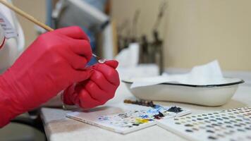 Laboratory worker painting eye prosthesis. Master in red latex gloves making artificial eye with a brush in clinic. Close-up. video