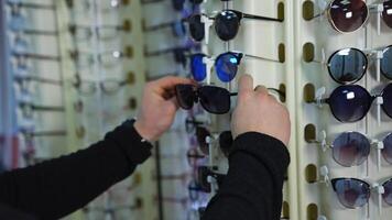 Fashionable sunglasses on stand at optics. Man testing new glasses in the shop. Buyer choosing eyewear in optical store. video