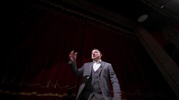 Theatrical man on stage. Performer in a suit moving on stage on red curtains background. Professional actor performing in theater. View from below. video