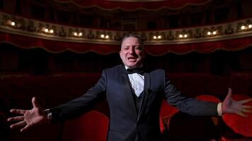 Happy actor in dark theatrical hall. Talented man in suit standing among vacant red chairs and shouting cheerfully. Portrait of a comedian in empty theater. video