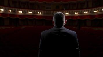 Performer man in front of empty auditorium. Man in suit taking off medical mask from is face and starts speaking while standing on stage in theater. Circling view. video