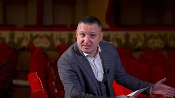 Portrait of an actor during the rehearsal. Man in suit sitting in a theater hall and performing a monologue while holding a script. video