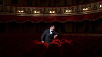 Disappointed actor in empty theatrical hall. Man in costume standing among vacant red seats and calling someone. No audience in opera house. Pandemic in the world. video
