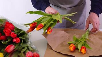 Gentle tulip bouquet assembly, hands arrange vibrant floral display on brown paper video