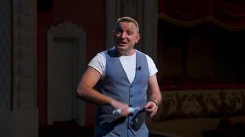 Presenter on stage. Man holding medical mask in his hand and talking on camera in empty theater. Portrait of middle-aged man speaker. Pandemic concept. video