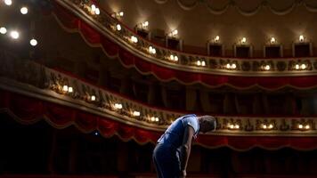 Actor bowing on theatrical stage. Man is standing on the scene of the classical theater and acting his role during the rehearsal before the empty hall. Back view. video