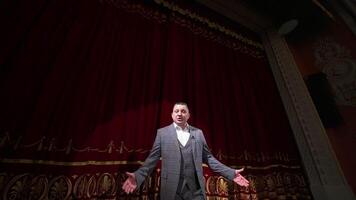 Theater host on red curtains background. Man in grey costume talking on a big stage. Portrait of an actor performing on stage. video