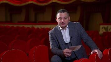 Man in costume reads a script. Medium shot of an actor rehearsing in empty theater among red chairs. Acting lifestyle. video