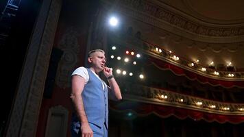 Smiling actor on stage. Middle-aged man standing on the scene of a theater and talking to the audience. Acting at bright spotlights. Side view. video