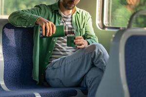 Man hands fill mug with tea from thermos while riding electric train for long commute. Long travel photo