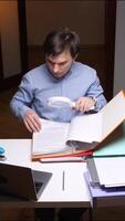 vertical Office worker examining documents with magnifying glass at desk video