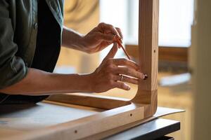Carpenter hands carefully screw bolts with hex key, securing table legs to woo tabletop in workshop photo