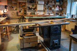 Tablesaw on workbench in carpentry workshop, shelves with tools and wood planks for furniture make photo