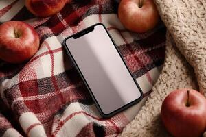 A smartphone on a red plaid blanket with apples and knitted fabric in warm, soft lighting. Great for autumn-themed promotions, lifestyle scenes, and mobile app mockups. photo