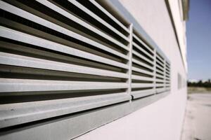 A metal ventilation grille mounted on the wall of a modern industrial building. Great for illustrating concepts of airflow, HVAC systems, construction, and urban infrastructure. photo