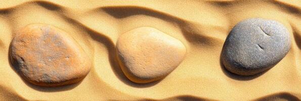 Three smooth stones resting on golden sand with wave patterns reflecting nature's texture photo
