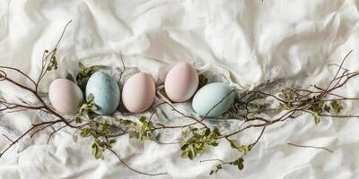 Pastel-colored easter eggs with greenery on soft white fabric backdrop photo
