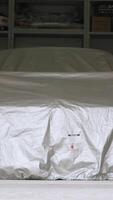 A sports car is parked under an awning in a bright home garage. Footage. Opens the gates of a white garage, inside a car closed with a cloth and shelves with a tool in the background video