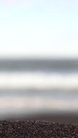 Close-up of dark colored sea sand or small pebbles. Footage. Blurred background with sea waves. Static frame video