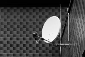 Brushed metal satellite dish rests against a textured brick wall in shadowy tones at dawn, capturing the quiet of early morning photo