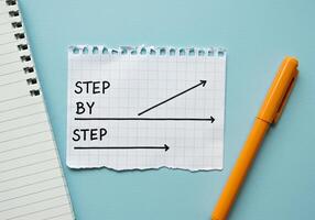 Step by step concept with arrow on paper, notebook and pen on blue background photo