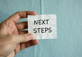 A person holding a piece of paper with the word next steps written on it photo