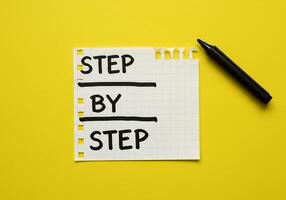 Step by step written on a piece of paper with a pen on yellow background photo