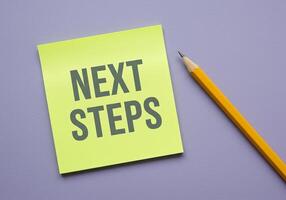Next steps on a yellow sticky note with a pencil on a purple background photo