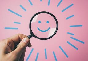 Hand holding magnifying glass over smiling face on pink background photo