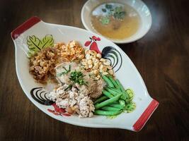 A white noodle with minced pork, pork skin sliced yardlong bean with shredded culantro in chiecken pattern dish on wood table texture photo