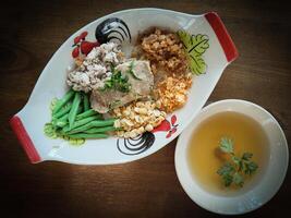 Thai Cha-Kang-Rao, a white noodle with minced pork, pork skin sliced yardlong bean with shredded culantro in chiecken pattern dish on wood table texture photo