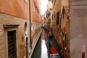 Typical narrow street and canals between Colorful and shabby houses in Venice, Italy. Historical architecture in Venice, parked boats on the canal. photo