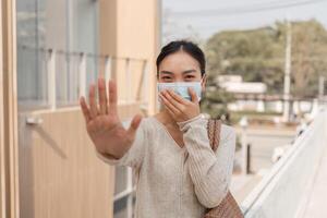 Diverse woman in a mask signaling stop while smiling outdoors in an urban setting. photo