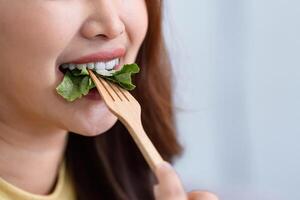 Healthy Eating and Close-Up Cooking. A woman taking a bite of fresh greens with a wooden fork. photo