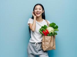 Happy asian woman holding a paper bag with vegetables and talking on the phone photo