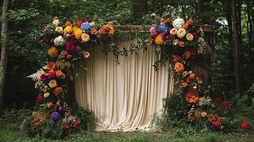 Luxurious Forest Wedding Ceremony Backdrop with Wooden Arch, Cream Drapery, and Vibrant Wildflower Arrangement Featuring Multicolored Roses, Hydrangeas, and Seasonal Blooms photo