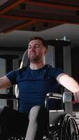 Man in a wheelchair performs lateral dumbbell raises during gym workout video