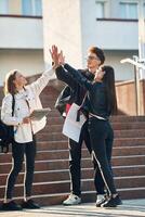 Giving high five to each other. Three young students are outside the university outdoors photo