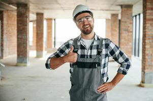 With thumb up. Construction worker in uniform in empty unfinished room photo