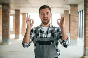 Showing, okay hands gesture signs. Construction worker in uniform in empty unfinished room photo