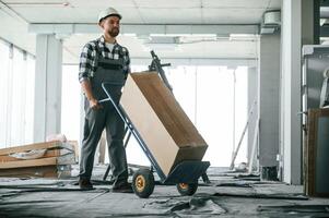 Transporting long paper box. Construction, worker in uniform in empty unfinished room photo
