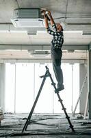 Standing on the, ladder. Repairman in uniform is in the unfinished building photo