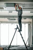 Standing, on, the ladder. Repairman in uniform is in the unfinished building photo